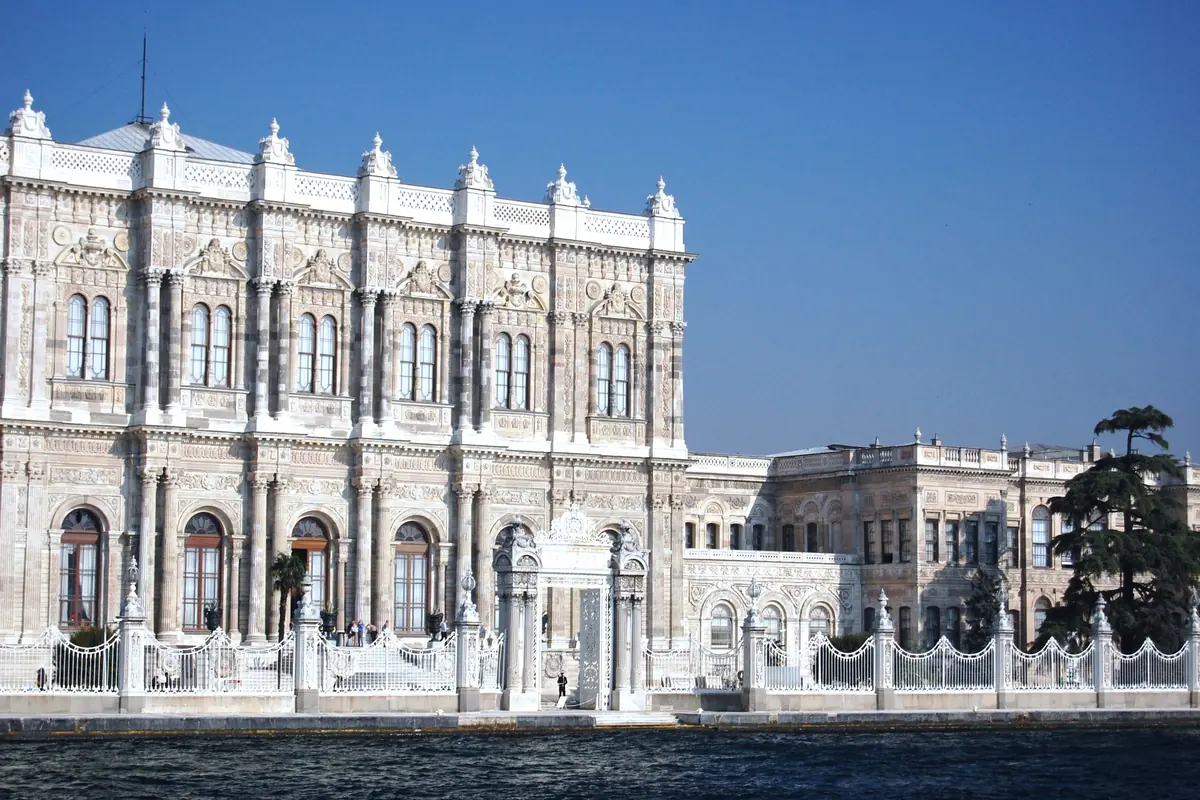 The central block of the palace's pale stone façade under a clear blue sky, with ornate windows and white railings.