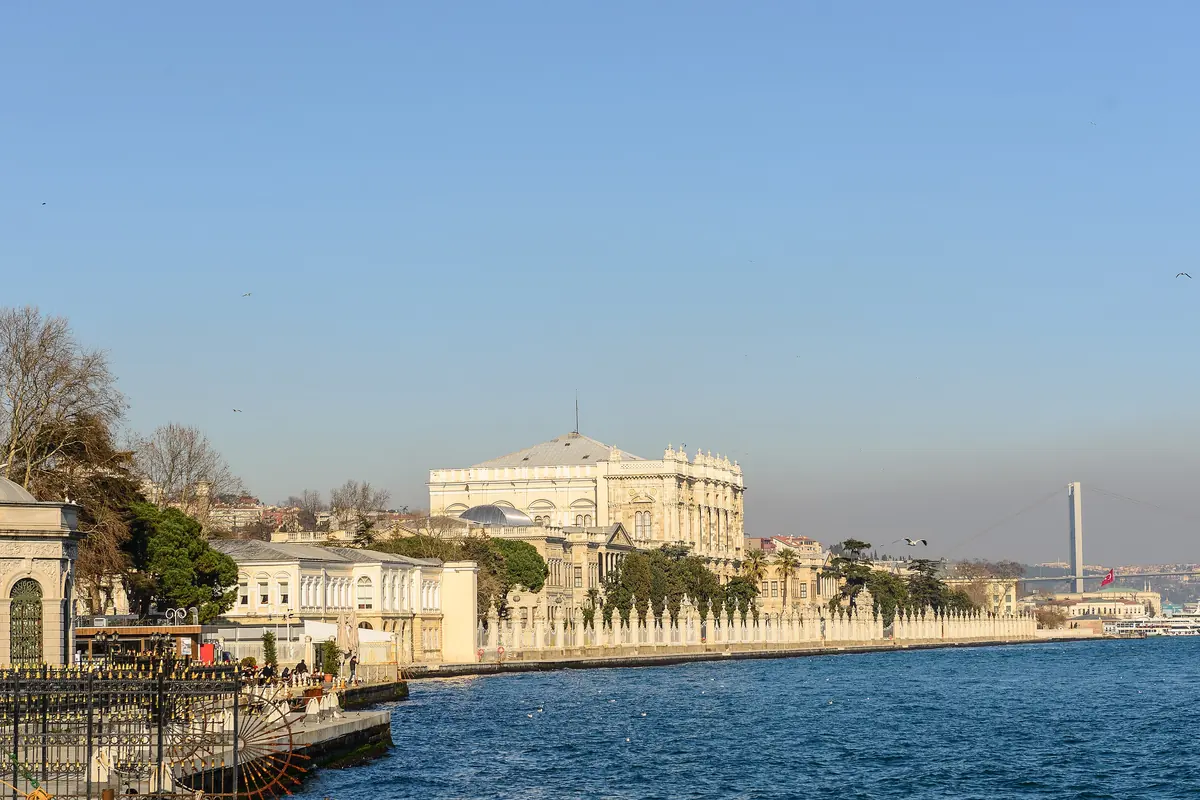 Dolmabahçe Palace and the mosque beside it along the Bosphorus shore, with a bridge in the distance and a clear blue sky