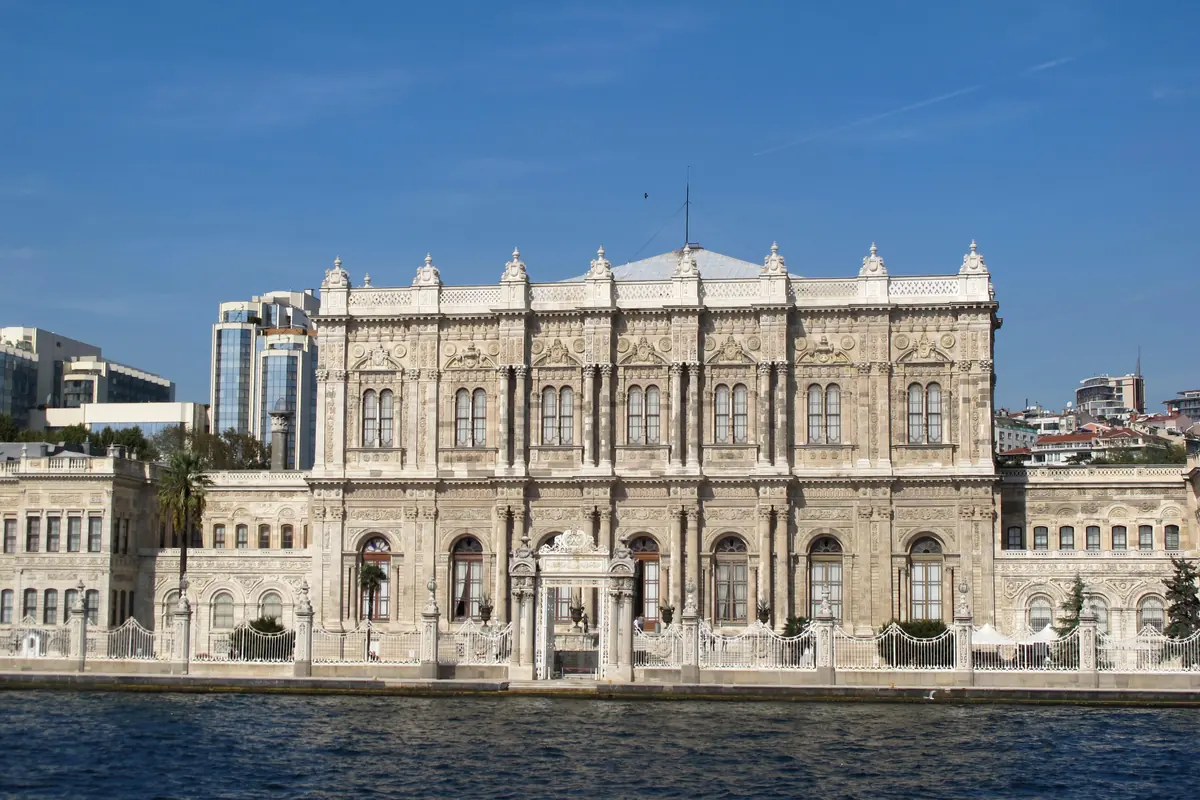 The central block of Dolmabahçe Palace's marble façade across the Bosphorus under a deep blue sky, with a white railing along the quay.