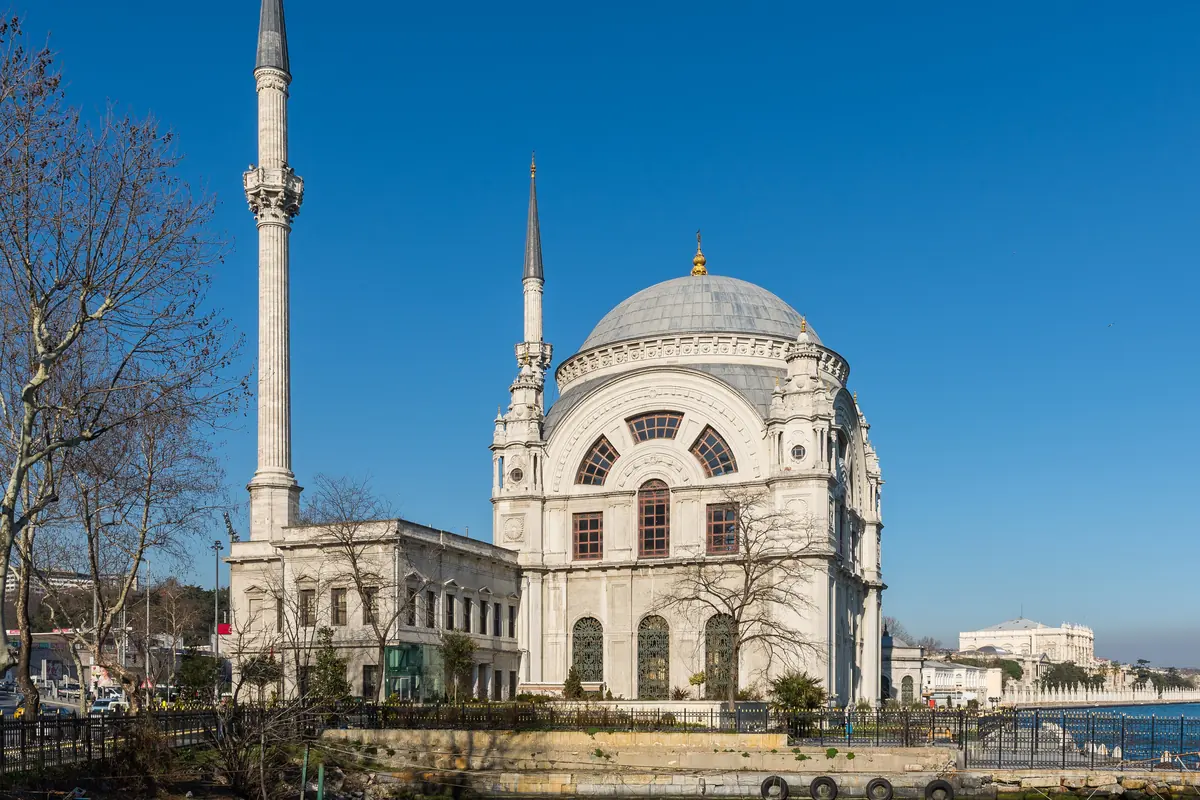 The white Dolmabahçe Mosque with its dome and two minarets beside the Bosphorus under a deep blue sky.