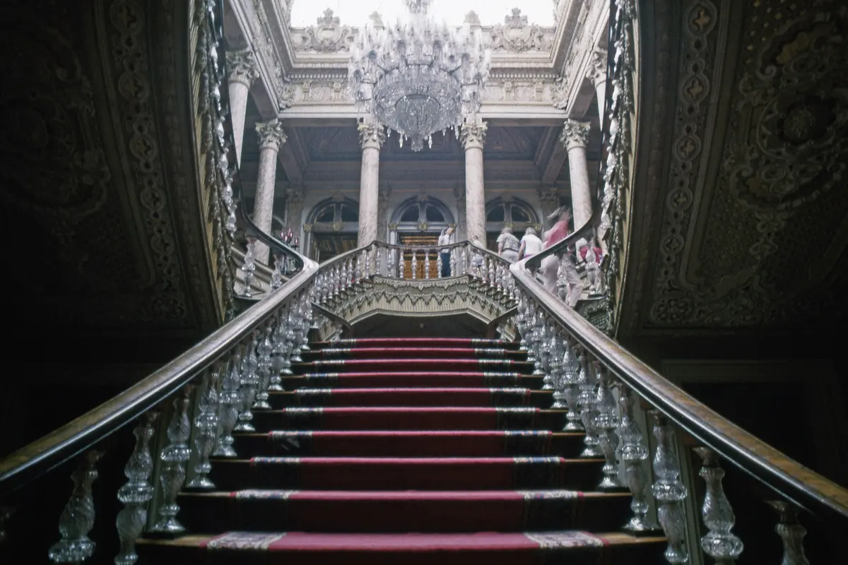 The double-horseshoe Crystal Staircase with a red carpet and glass balusters rising to a landing under a chandelier.