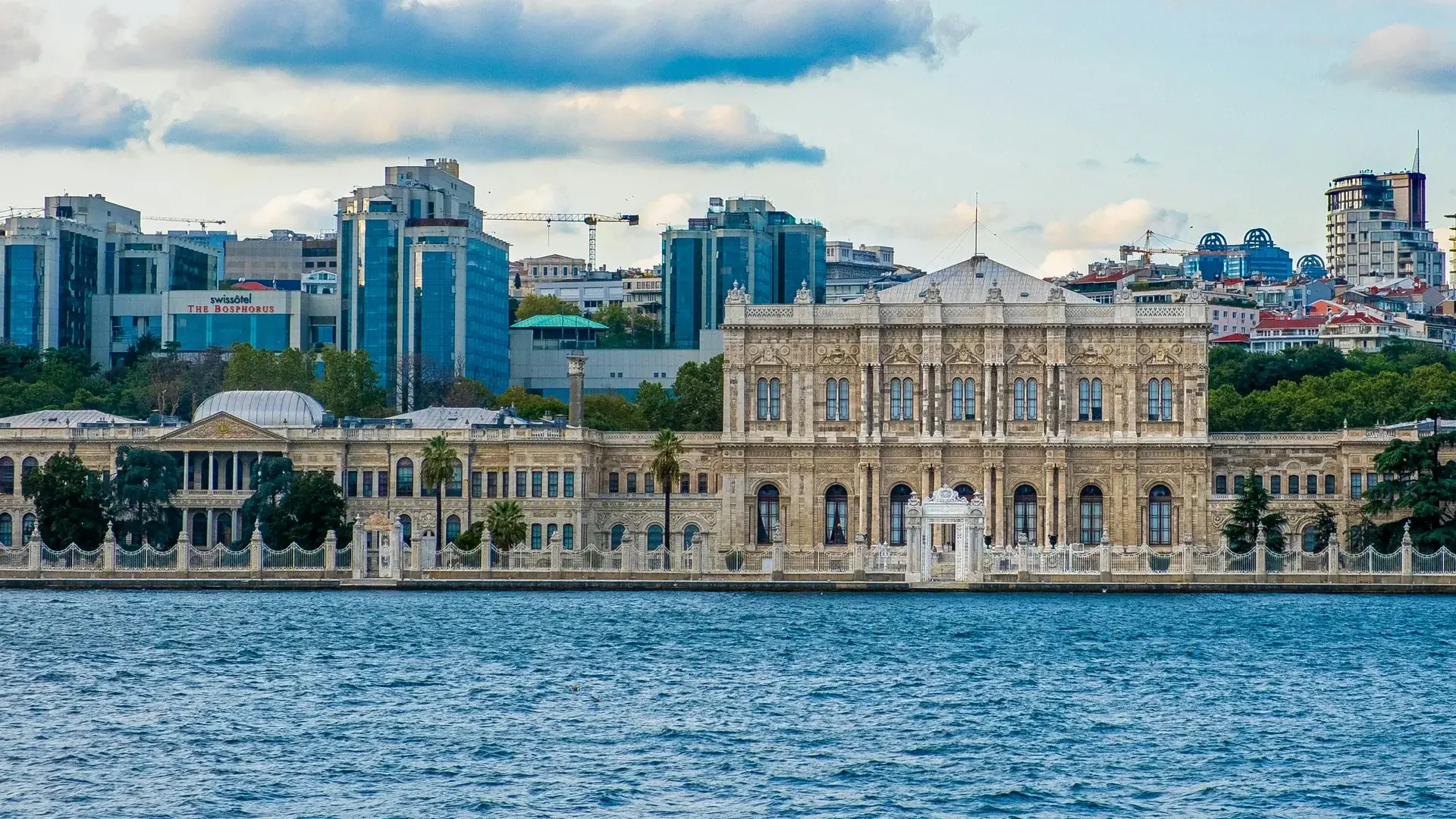Dolmabahçe Palace seen across the Bosphorus: the long marble façade with its central block, the white gate on the quay and blue water in front.